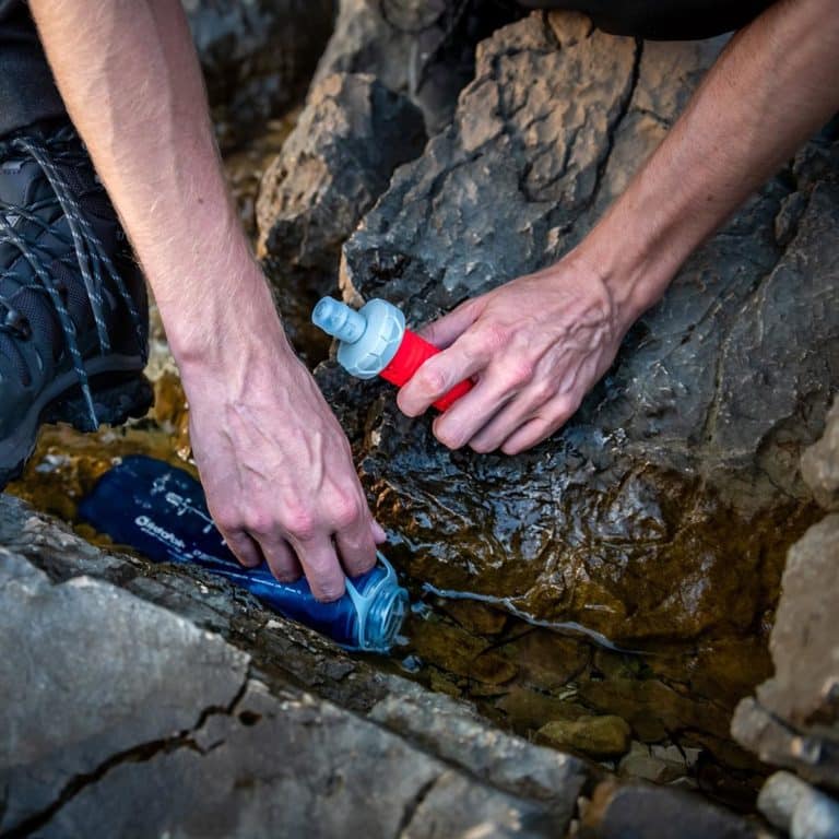 Personne qui tremple sa flasque d'eau dans un ruisseau.